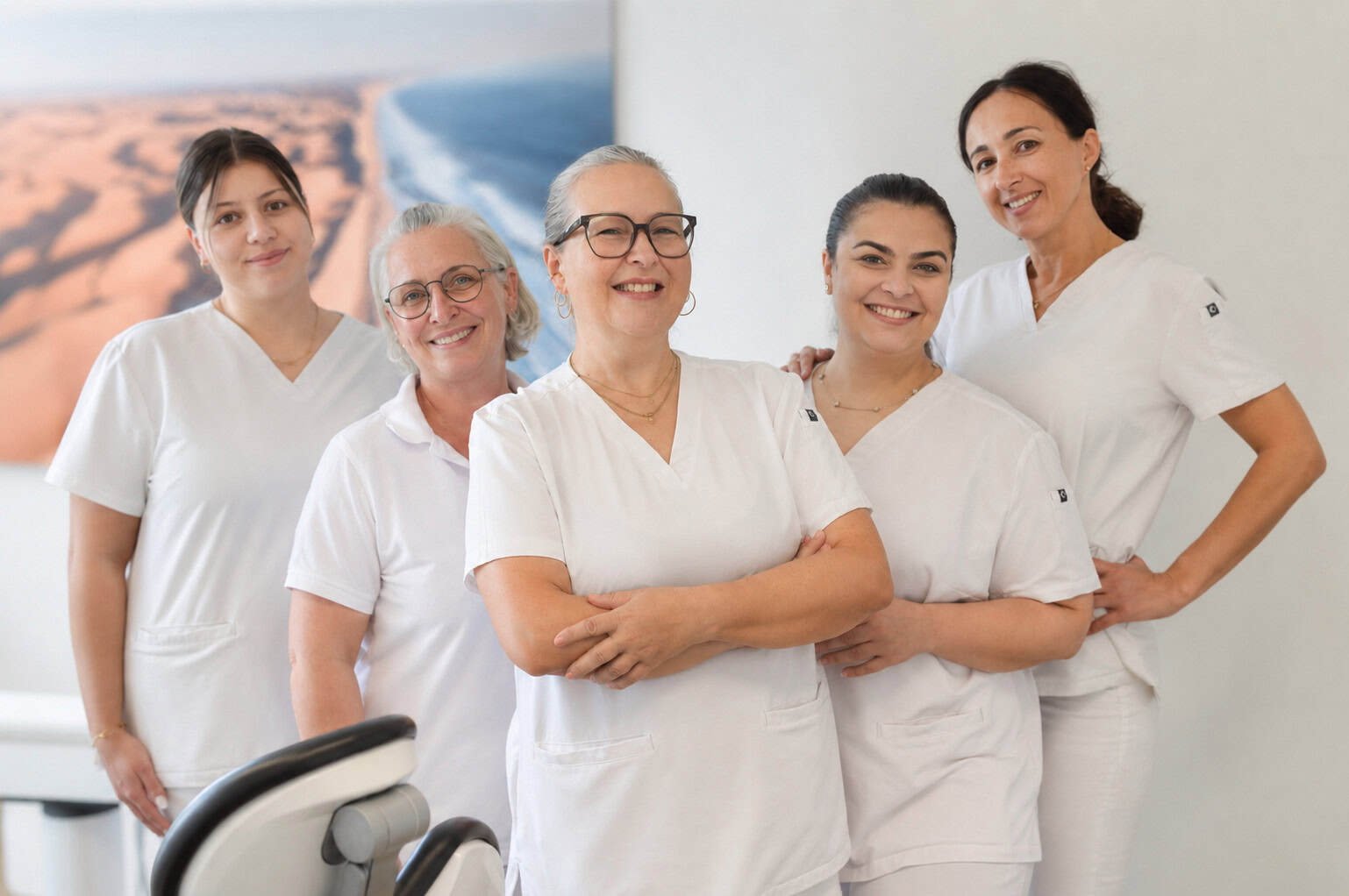 Lächelndes Prophylaxe-Team in weißen Kitteln bestehend aus fünf Mitarbeiterinnen in Zahnarztpraxis mit freundlicher Atmosphäre.