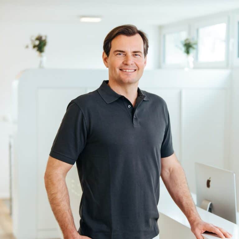 Lächelnder Mann in Zahnarztpraxis steht neben Computer.