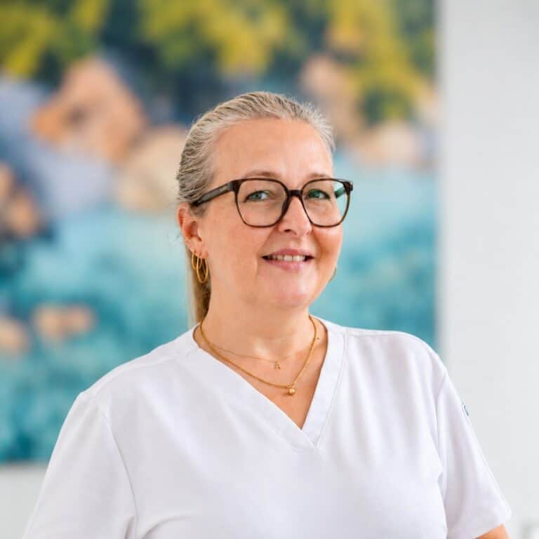 Professionelles Porträt einer Frau mit grauen Haaren, Brille und freundlichem Lächeln. Gezeigt wird Anja Lück, die Team-Leitung Prophylaxe bei BaumstiegerZahnärzte.