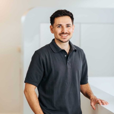 Lächelnder Mann in dunklem Poloshirt und mit dunklem Haar.