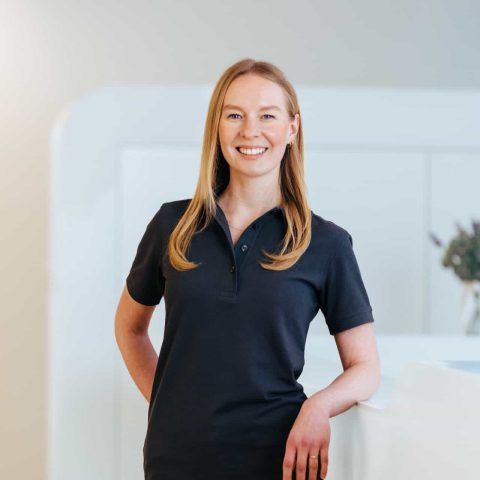 Lächelnde Frau in dunklem Poloshirt steht in Praxis.